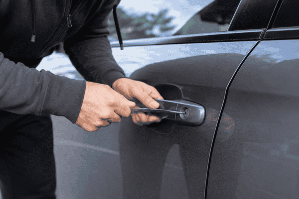 Person attempting to force open a locked car door with a metal tool before an emergency locksmith arrives in Mississauga.